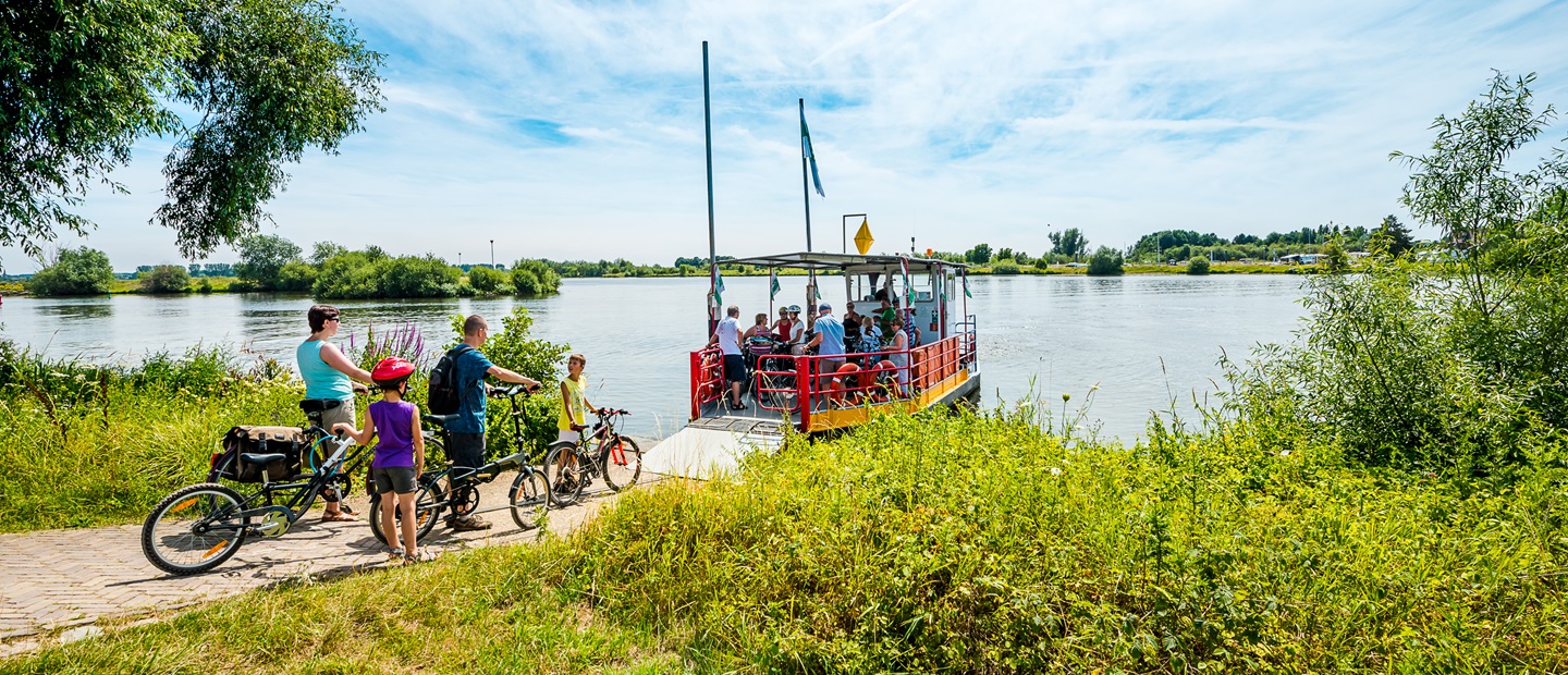 Fietsers wachten met hun fietsen op een veerpont om de Maas over te steken in Hart van Limburg.