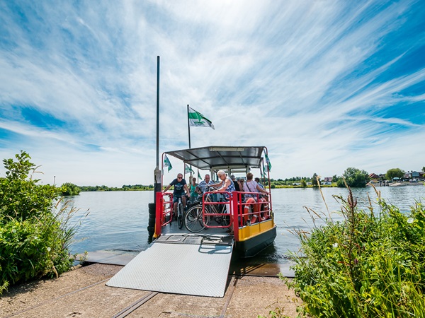 Veerpont op de Maas met fietsers die klaarstaan voor de oversteek in Hart van Limburg.