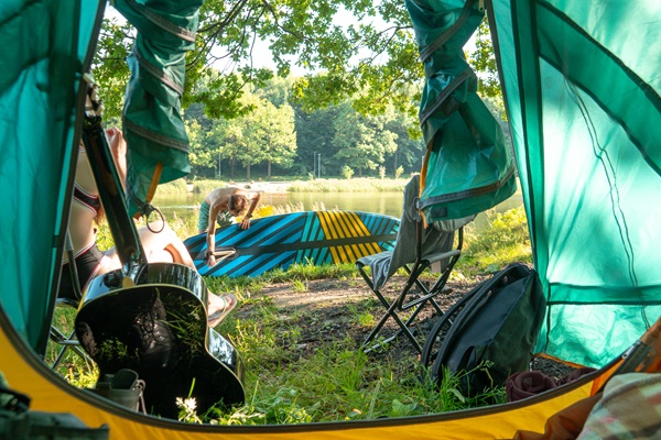 Jongen maakt zich klaar om te gaan suppen terwijl vriendin voor de tent zit op een camping