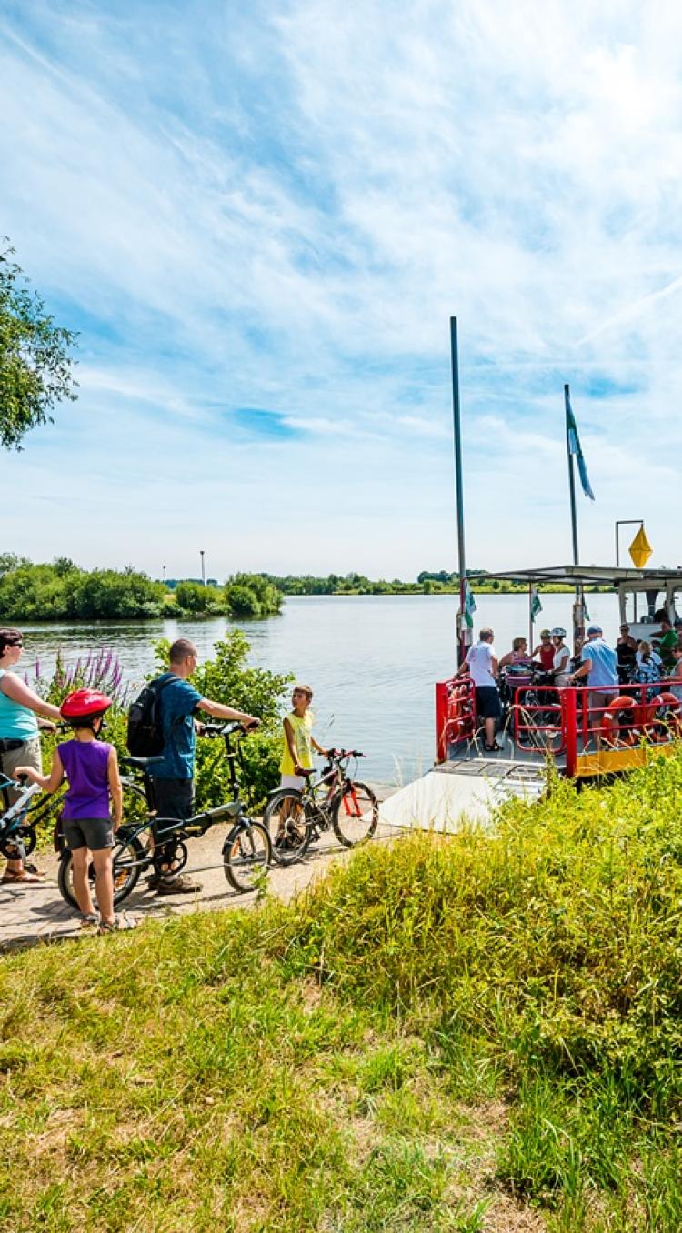 Fietsers wachten met hun fietsen op een veerpont om de Maas over te steken in Hart van Limburg.