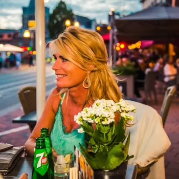 Vrouw geniet van een drankje op een sfeervol terras op de Roerkade in Roermond tijdens de avondschemering.