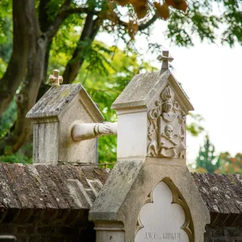 Historisch grafmonument met stenen kruisen en versieringen, omringd door groen en oude bomen.