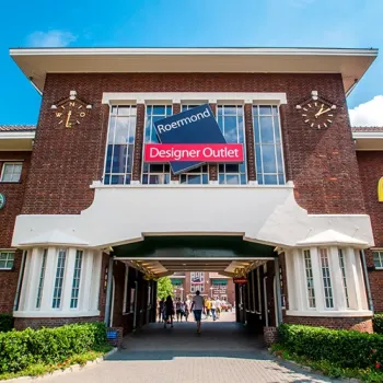 Entree van Designer Outlet Roermond in het voormalige kazerneterrein, met de historische bakstenen poort en het Designer Outlet-bord erboven.