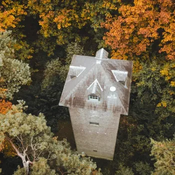 Luchtfoto van een stenen Uilentoren op Landgoed de Bedelaar in Leudal tussen bomen met groene en oranje herfstbladeren.